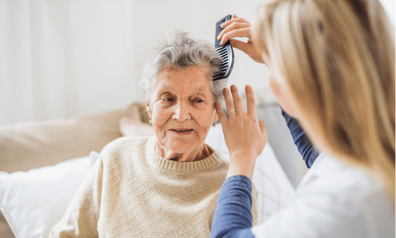 Vermittelte Pflegekraft kämmt Dame die Haare